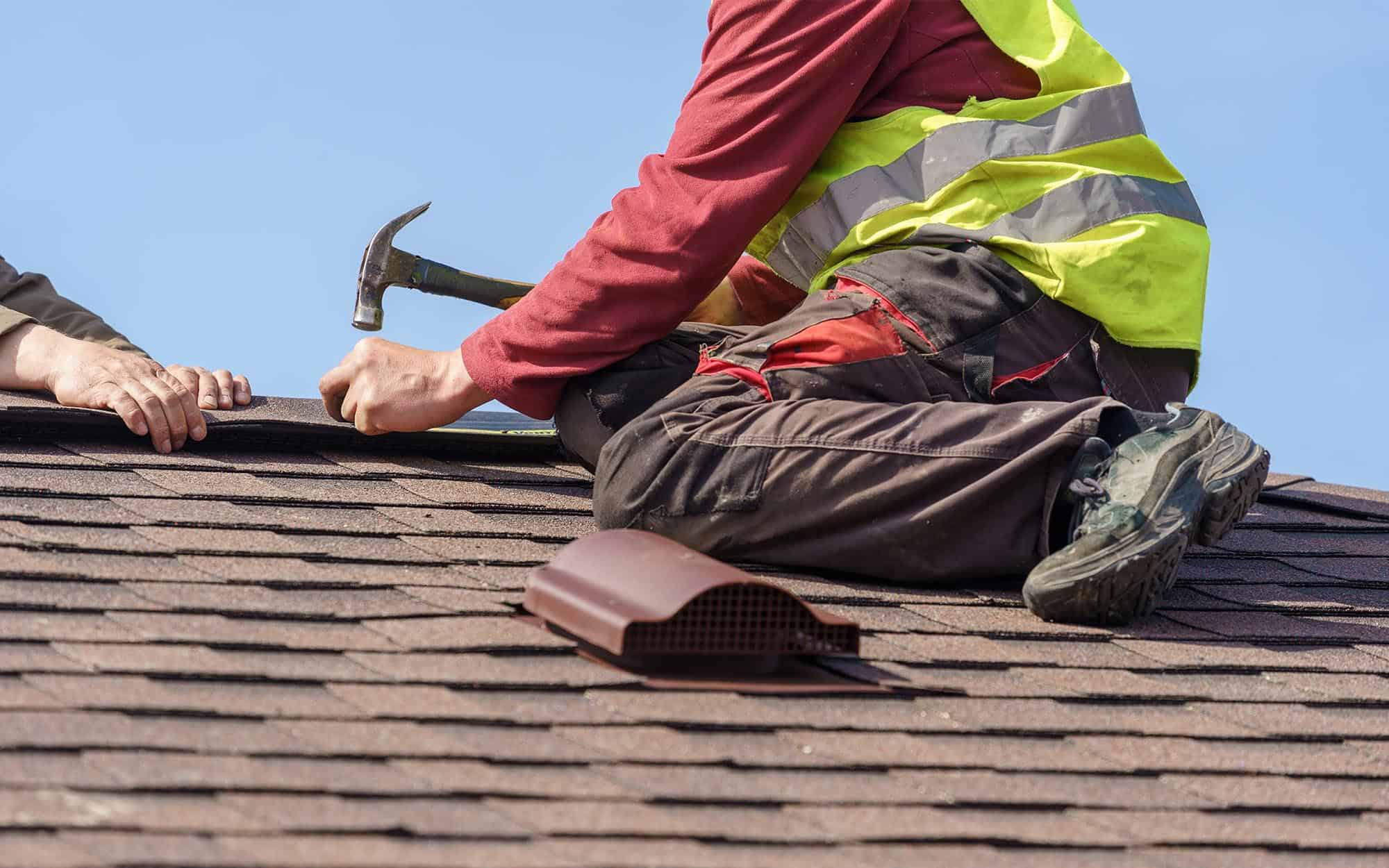 Side view of a man nailing shingles to a roof