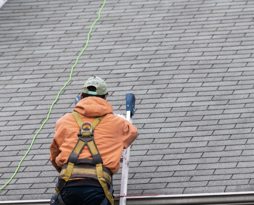 House during day with gray color Single Family Home and man walking on roof shingles and ladder during repair